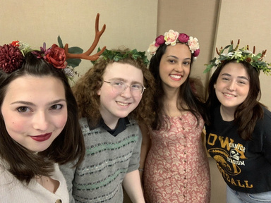 four students standing in a row, smiling, leaning towards camera