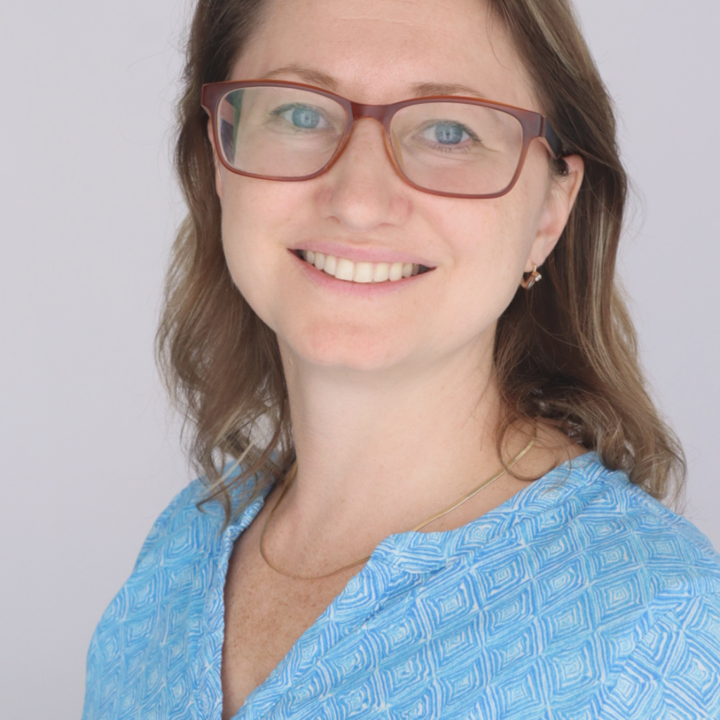 female presenting individual with a light blue top and brown-red glasses