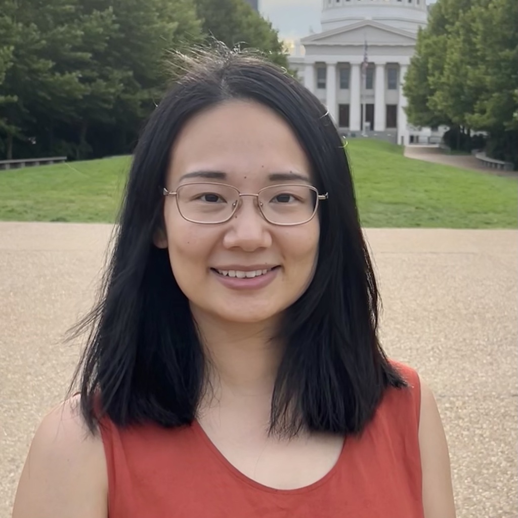female presenting individual with dark hair, glasses, and an orange top