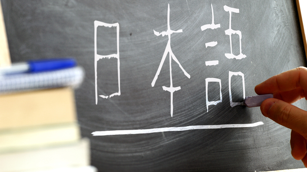 A hand writing Japanese characters on a blackboard.