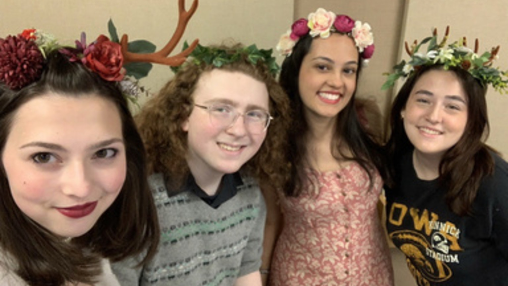 four students standing in a row, smiling, leaning towards camera